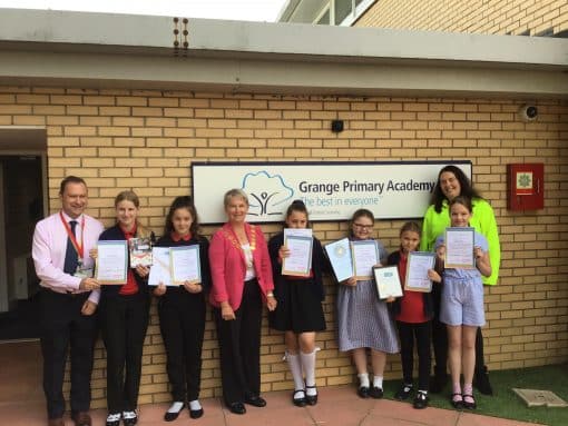School children outside school sign with awards.